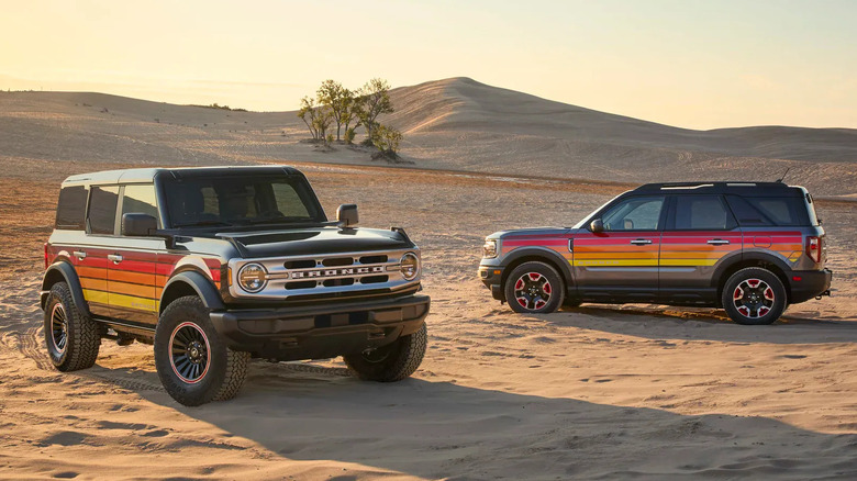 Two Ford Bronco SUVs with retro sunset stripe graphics parked on a sandy desert landscape.