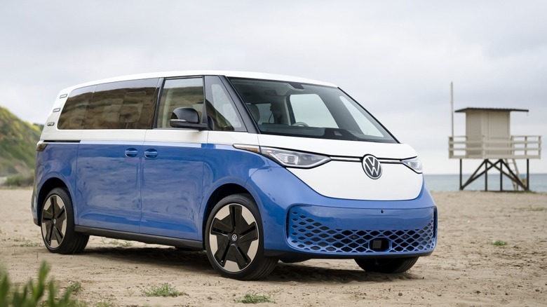 A blue and white Volkswagen ID. Buzz, an electric van, parked on a sandy beach.