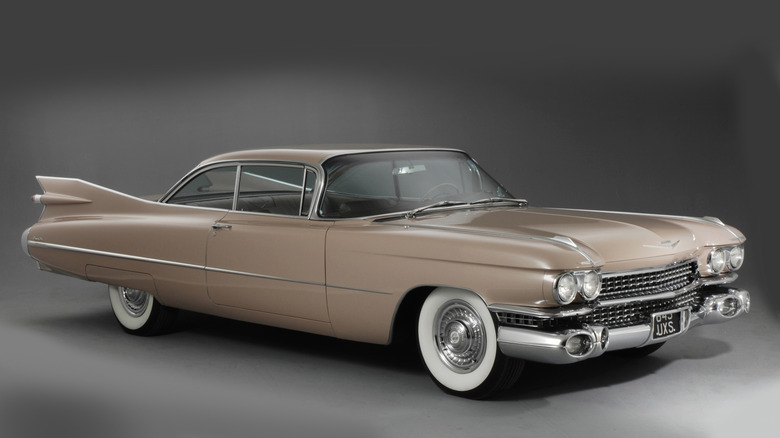 A classic beige Cadillac Coupe de Ville with iconic tailfins, whitewall tires, and chrome accents.
