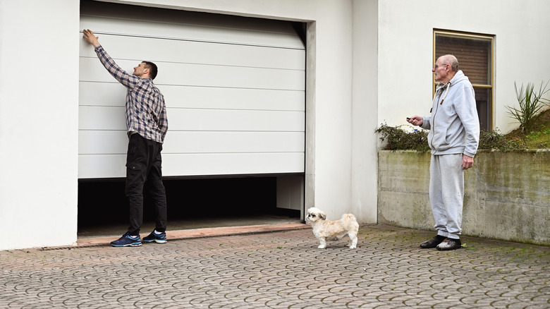 Two men and a dog repair a half-open garage door.