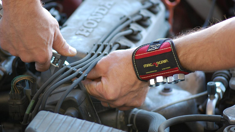 A mechanic using a magnetic wristband to hold bolts