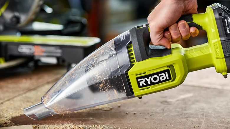 A man using a Ryobi hand vacuum to clean up sawdust on a work bench