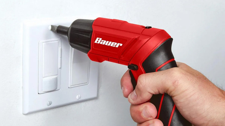 A man using an electric screwdriver on a light switch.