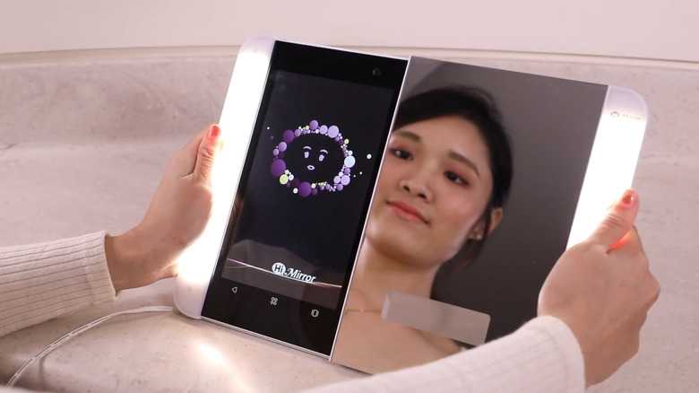 A woman looking at her reflection in the HiMirror Slide, with the device tablet being in the extended position.
