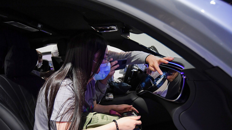 A Mercedes-Benz EQS car that is equipped with the MBUX hyperscreen with two people sitting up front.
