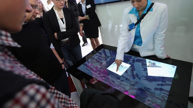 A hostess displaying how the Samsung SUR40 table works to a crowd of onlookers at the CeBET trade show in 2013.