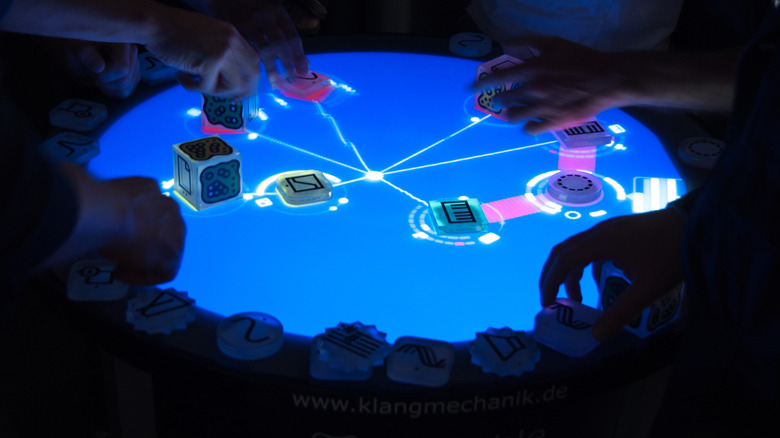 The Reactable circular music table with some blocks already placed on it in a dark room.