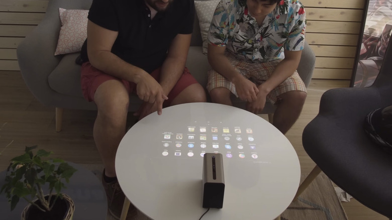 Two men sitting on a gray couch, interacting with the projection from a Sony Xperia on a small, round, white table in front of them.