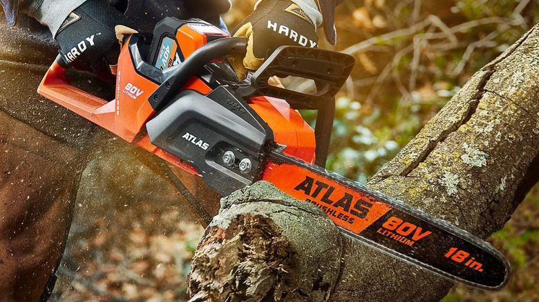 A person cutting a tree log with an Atlas 80V chainsaw
