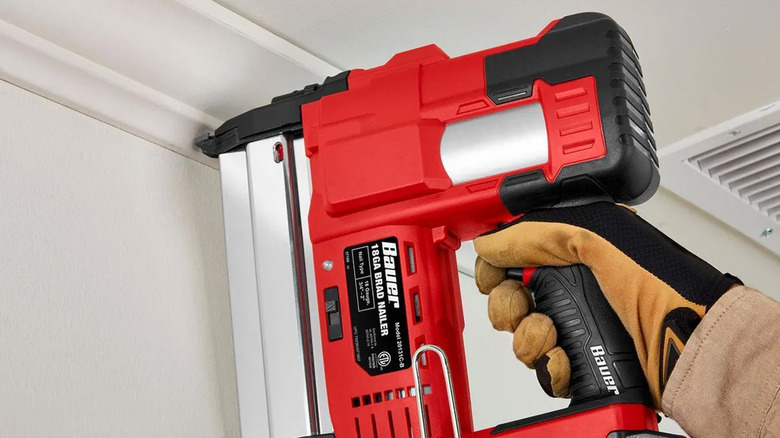 A worker using a Bauer nail gun to attach a piece of trim to a wall.