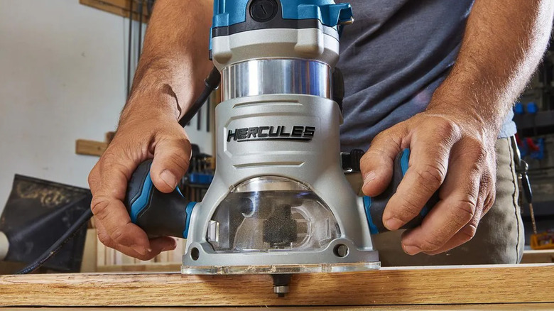 A person out of frame using a Hercules fixed base router on a piece of wood.