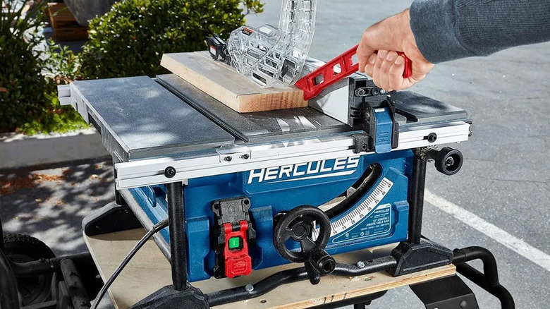 A person pushing a piece of wood on a Hercules table saw with a push block.
