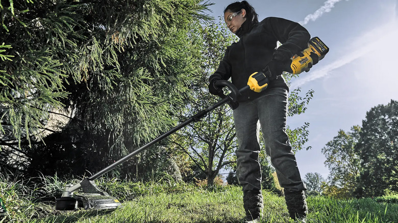 A woman using a string trimmer to cut weeds.