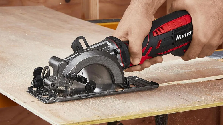 A person using a Bauer brand circular saw to cut a piece of plywood.