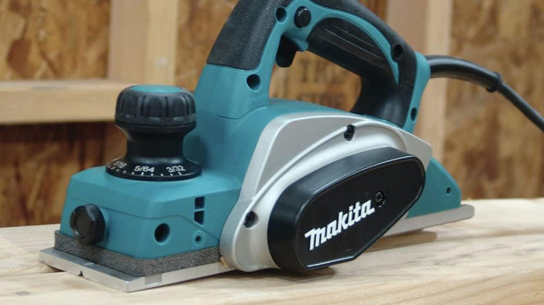 A Makita corded planar on a piece of wood in a workshop.