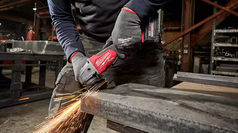 A worker using a Milwaukee angle grinder on a piece of metal