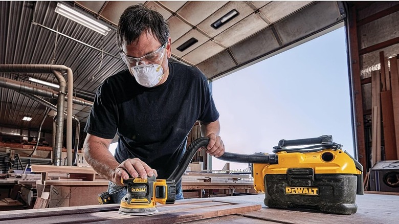 Man sanding wooden surface with an orbital sander connected to a vacuum