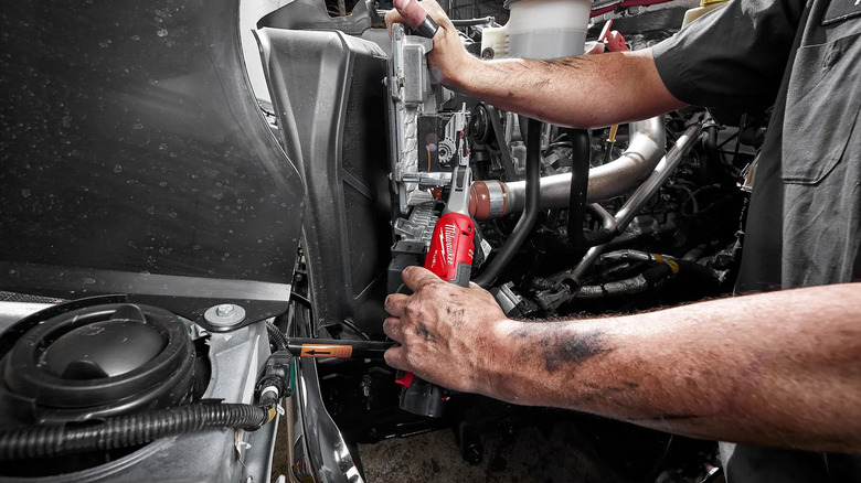 A man using a Milwaukee cordless ratchet to fix a car.