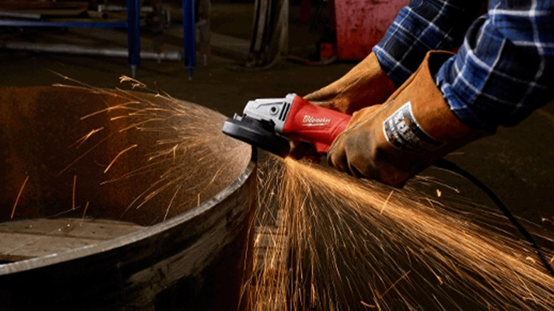 A gloved worked using an angle grinder on a large, round piece of metal.