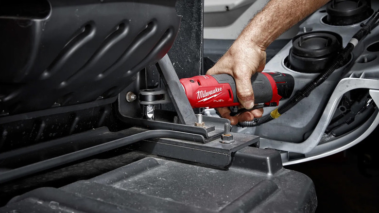 A man using a Milwaukee cordless ratchet on an automobile repair.