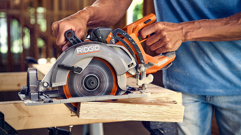 A man cutting a piece of wood with a Ridgid circular saw.