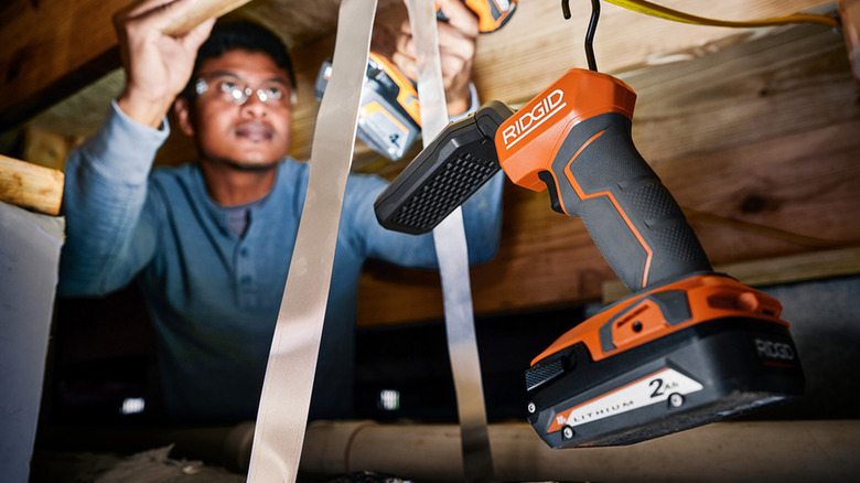 A man working under a house with a Ridgid LED Stick Light to help.