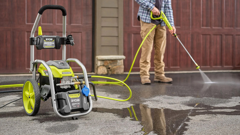 A man pressure washing his driveway with a Ryobi pressure washer.