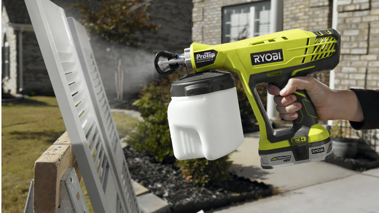 A person using a paint sprayer to spray house shutters