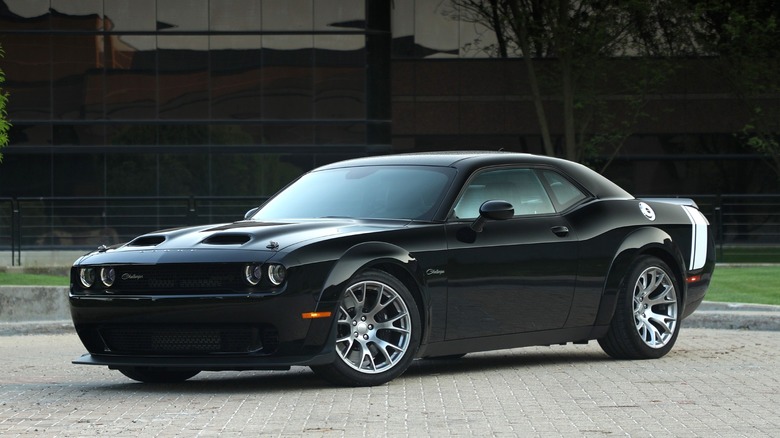 A 2023 Dodge Challenger SRT Black Ghost parked on a brick driveway in front of a dark glass building.