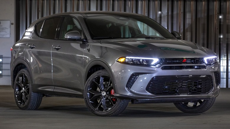 A 2023 Gray Cray Dodge Hornet GT is parked in a dimly lit garage with its LED headlights on.