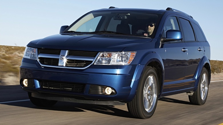A 2009 blue Dodge Journey is seen driving on an open highway under clear skies.