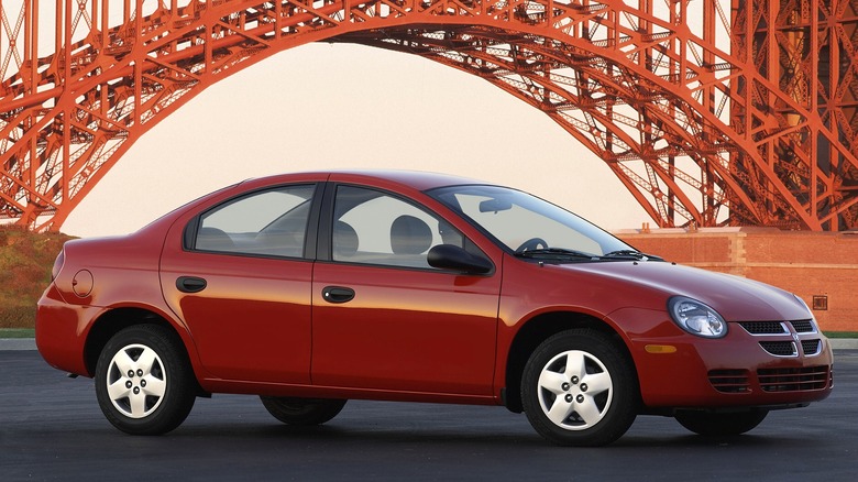 A red 2004 Dodge Neon SE is parked in front of a large red steel bridge structure.