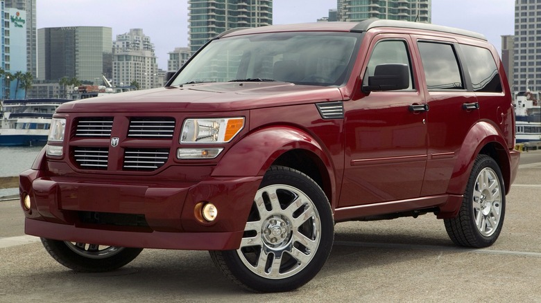 A 2007 red Dodge Nitro is parked in front of a city skyline and marina.