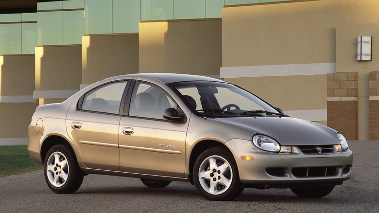 A 2002 beige Dodge Neon SE sedan parked in front of a modern building.
