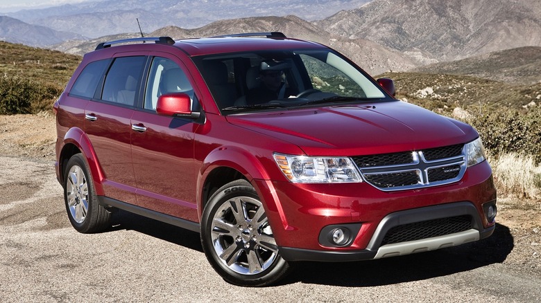 A 2013 red Dodge Journey SUV parked roadside with mountains in the background.