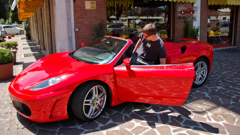 A person stooping low to get into their red Ferrari