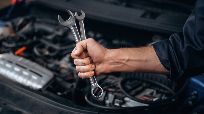 A mechanic gripping two spanners with a car engine in the background