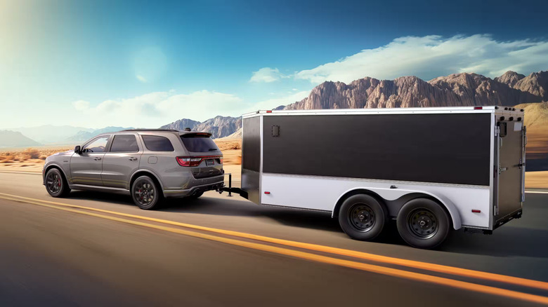 A gray 2026 Hellcat Jailbreak towing a midsize trailer on a desert highway
