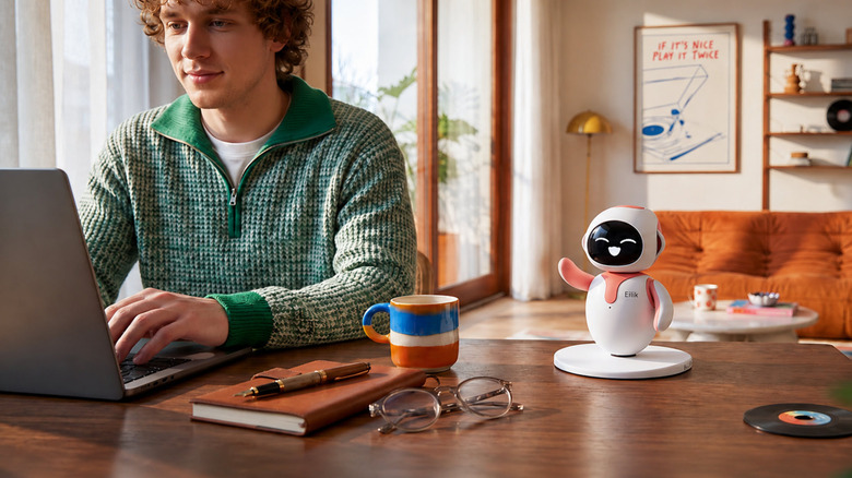 Man working on a laptop with an Eilik robot companion on the desk