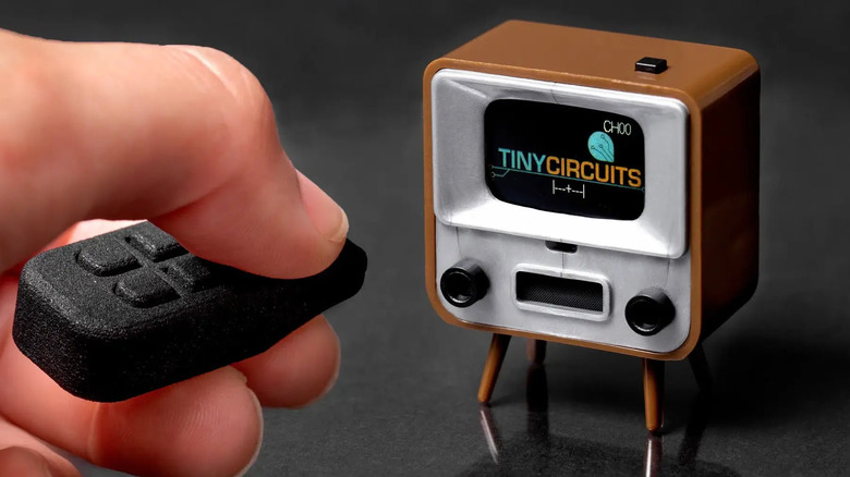 A tiny tv on desk with a person controlling it using a tiny remote controller