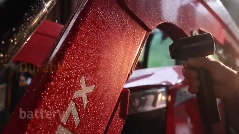 Hand using a mini blower to blast water from a red vehicle
