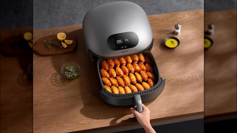 Hand removing a basket of chicken wings from a countertop cooking device