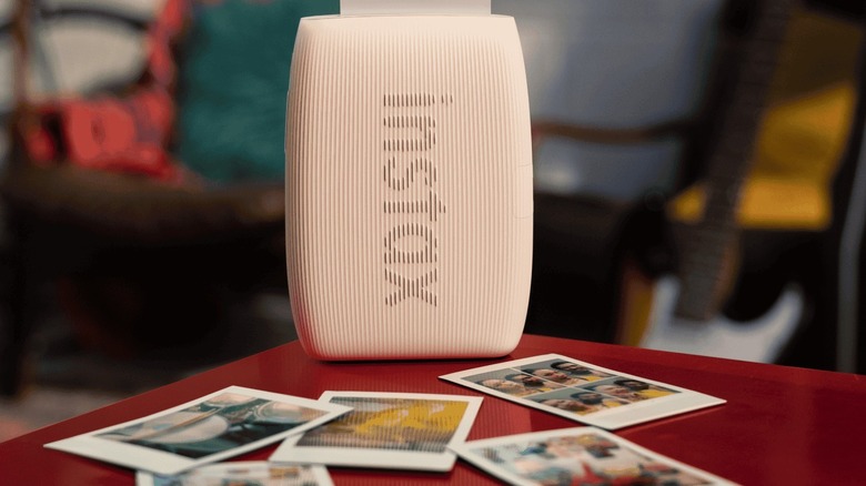 A Fujifilm Instax Mini Link 3 on a table with a handful of photographs