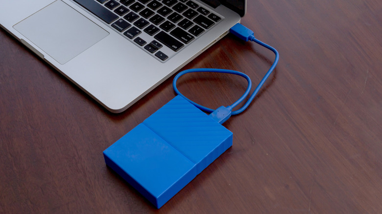 Blue portable external hard drive connected via USB to a silver laptop on a wooden desk.