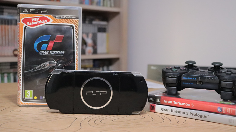 Black Sony PSP resting next to a PlayStation 3 controller and game cases.