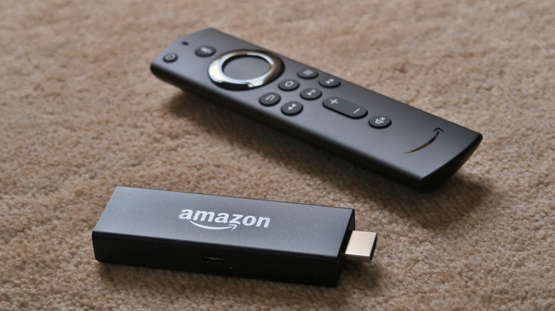 Black Amazon Fire TV Stick streaming media player with its remote control on a carpet.