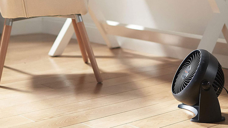 A black Honeywell fan placed on the floor beside a wooden chair