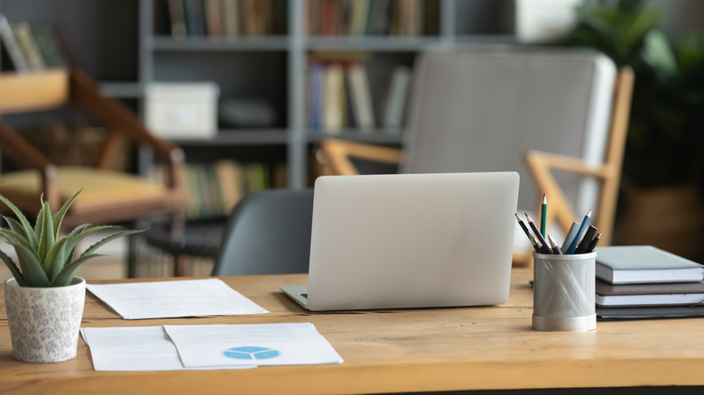 A laptop, books, papers, and a case of pencils sitting on a table in a home office