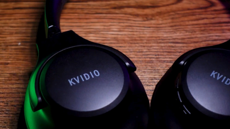 Black KVIDIO headphones resting on a table slightly illuminated by green light