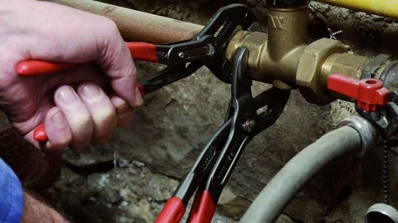 A worker using two Knipex Cobra pliers to turn a pipe fitting